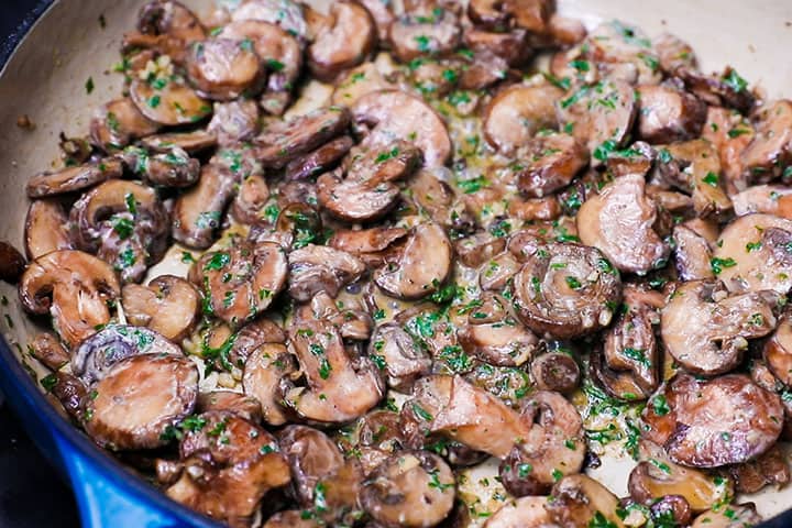 sautéed mushrooms in a pan with sour cream and chopped parsley