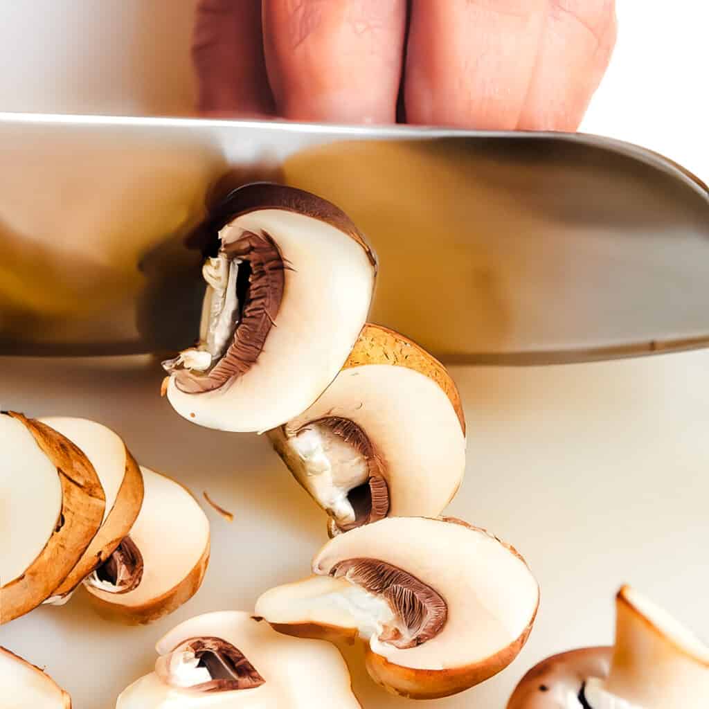 a knife slicing through a mushroom with more slices on the cutting board.