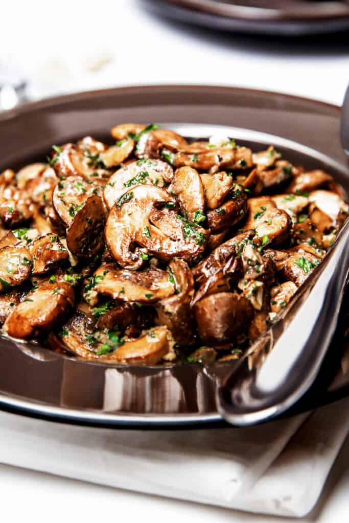 golden sautéed Mushrooms in a bowl with a serving spoon.