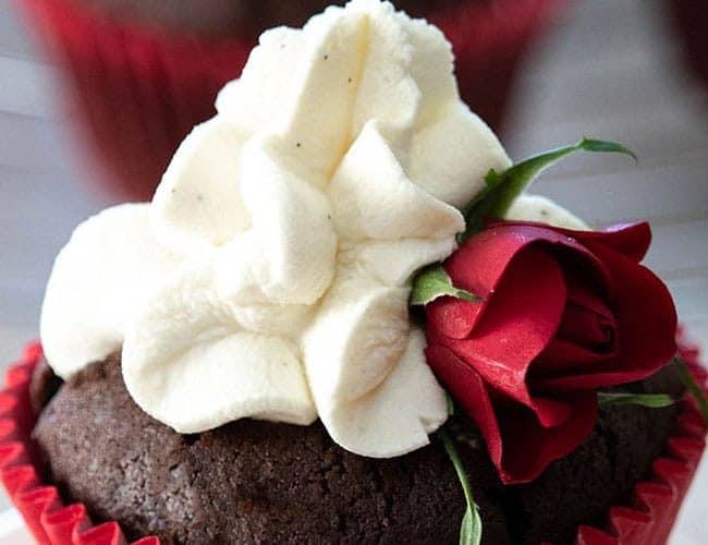 A chocolate cupcake with a red casing, whipped cream icing and a small red rose for decoration