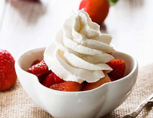 A bowl of strawberries topped with fresh whipped cream