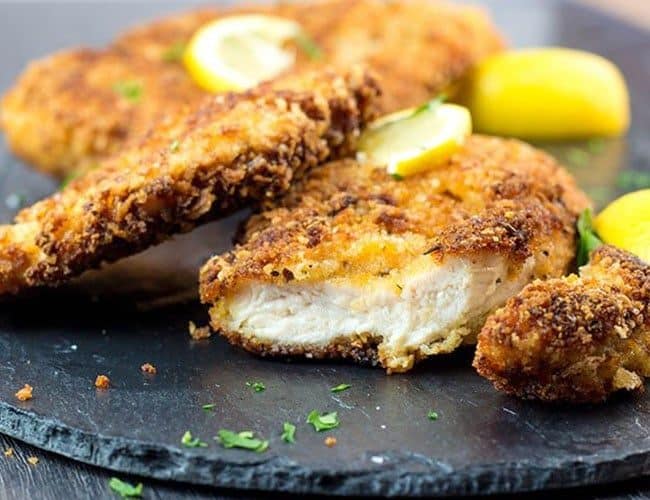 Crispy Breaded Chicken Cutlets on a dish with a piece cut off showing the juicy meat