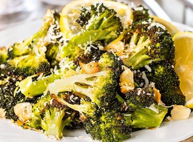 a close up of broccoli piles high on a plate scattered with grated cheese and brown garlic