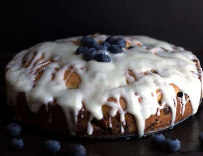 The Best Blueberry Cake EVER on a cake plate topped with fresh blueberries