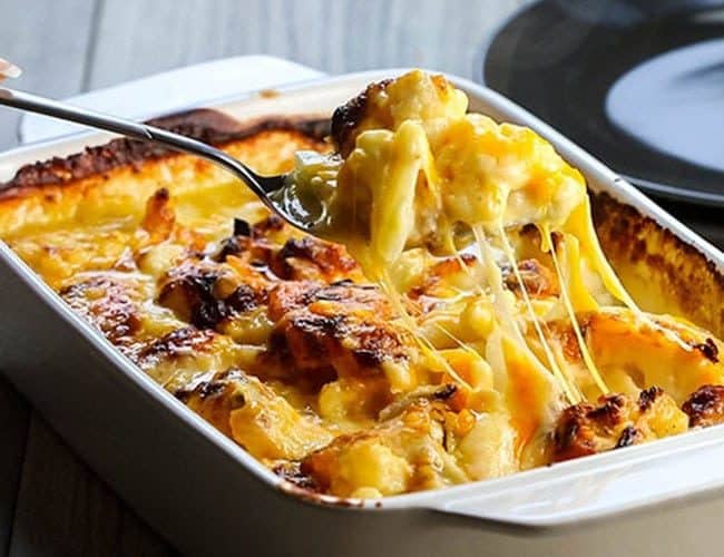 Cheesy Cauliflower Casserole being scooped from the pan with strings of cheese hanging from the spoon