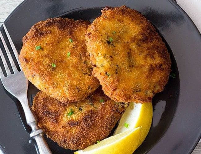 Three Crab Cakes on a plate with lemon wedges and a fork next to it