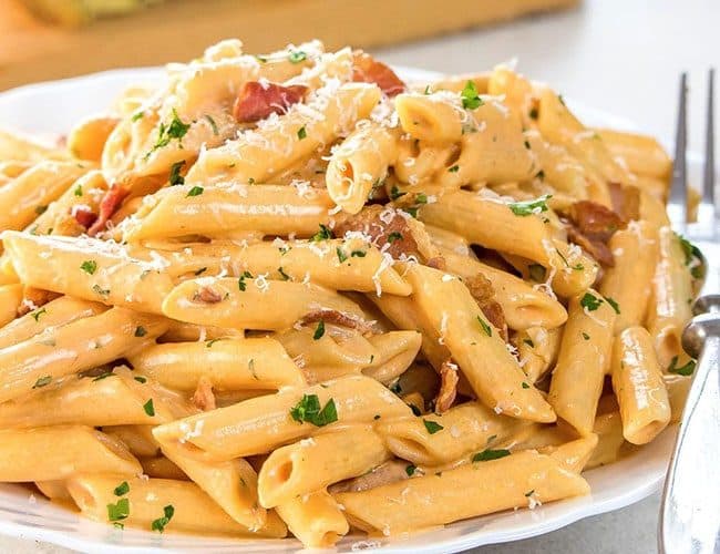 Penne Alla Vodka piled high on a white plate, sprinkled with parmasean cheese.