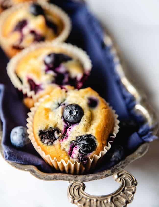 Five Blueberry muffins lined up on a silver tray with an ornate handle