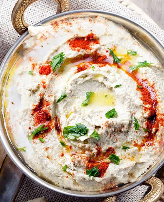 a plate of Baba Ghanouj garnished with olive oil, paprika and chopped parsley with bread next to it