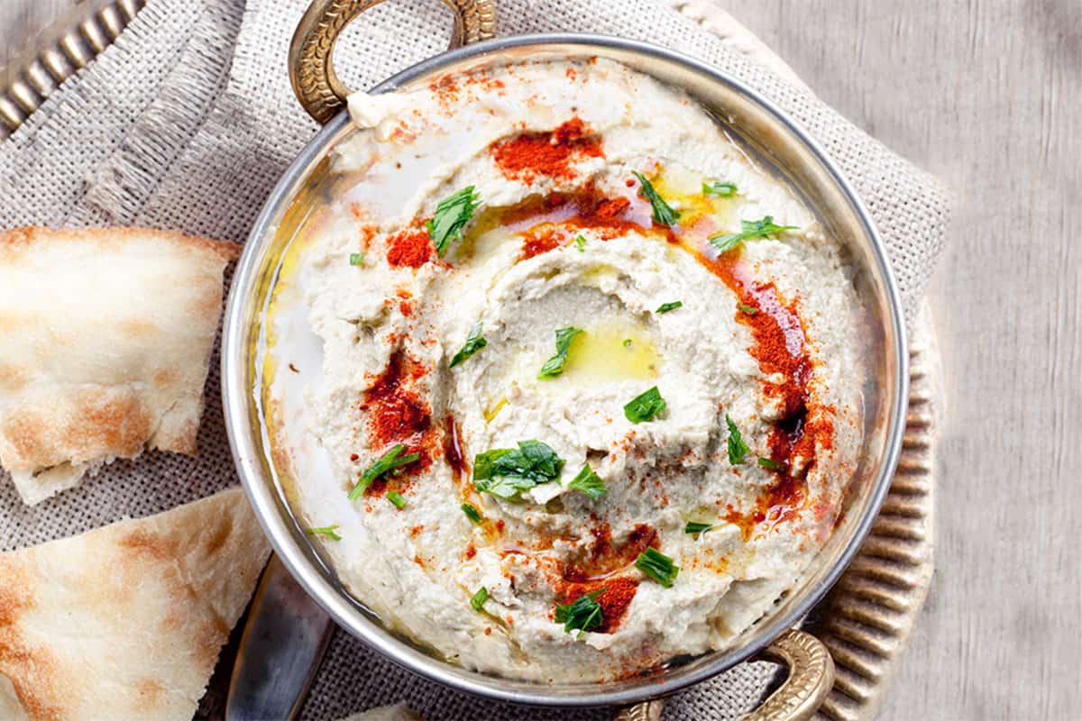 a plate of Baba Ghanouj garnished with olive oil, paprika and chopped parsley with bread next to it