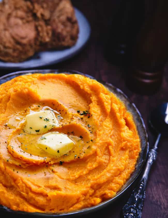 a dish of mashed sweetpotatoes topped with butter and ground black pepper