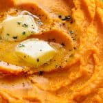 A dish of mashed sweet potatoes topped with butter and ground black pepper.