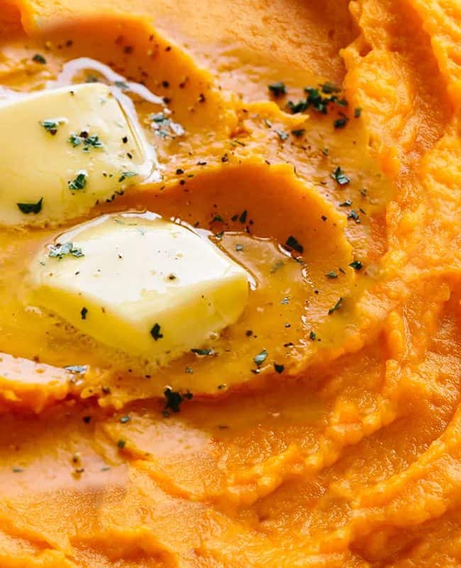 A dish of mashed sweet potatoes topped with butter and ground black pepper.