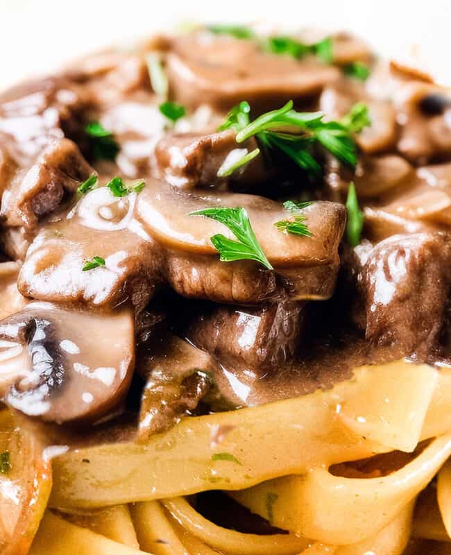 a close up image of Beef and mushrooms in a creamy Stroganoff sauce over noodles