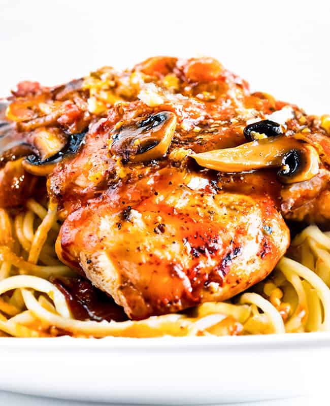 a close up image of Chicken Cacciatore on spaghetti with a glass of red wine in the background.