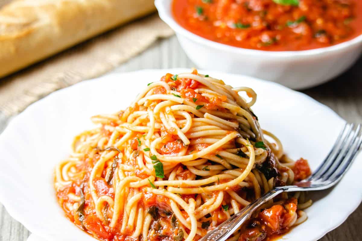 A plate of pasta with marinara sauce with a fork next to it and fresh basil near the dish