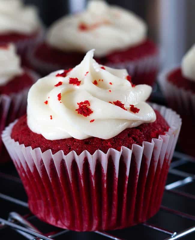 Red Cupcakes swirled with frosting and sprinkled with cake crumbs and more cupcakes in the background.