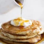 A stack of pancakes on a plate, with Cream and syrup