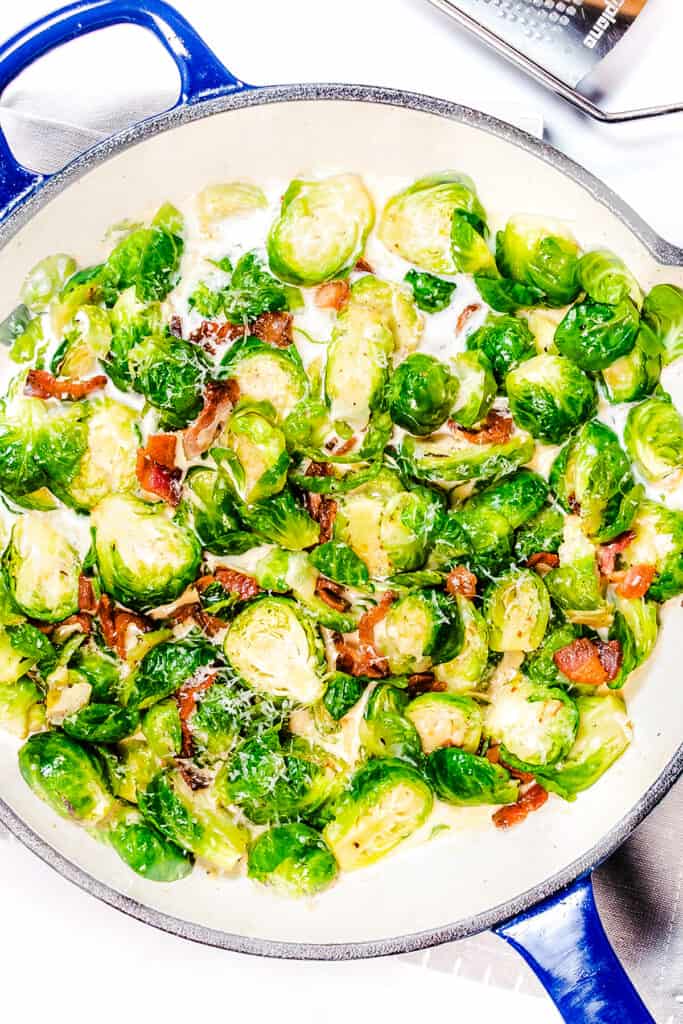 an overhead image of a pan with brussels sprouts and bacon in a cream sauce