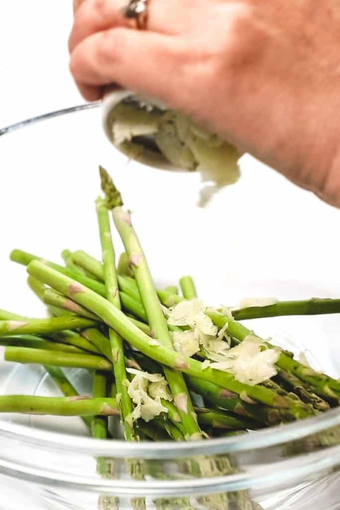 thin sliced garlic being added to a bowl with asparagus