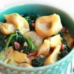 A bowl of Tortellini with cream sauce, spinach and bacon bits