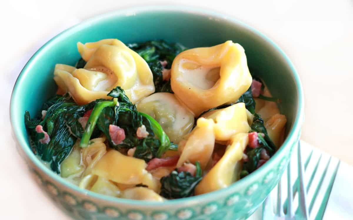 A bowl of Tortellini with cream sauce, spinach and bacon bits