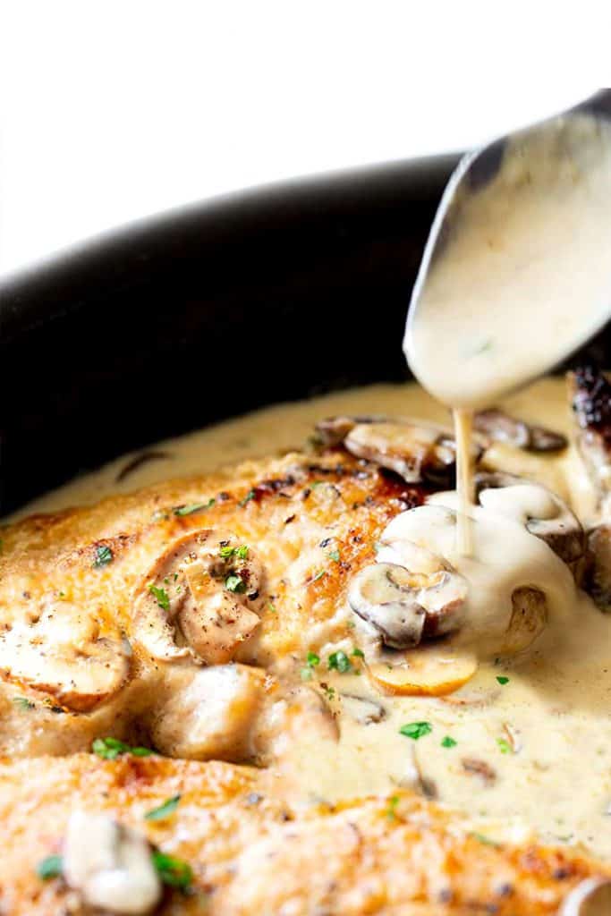 Creamy Mushroom Chicken in a skillet with a spoonful of sauce being served from it.