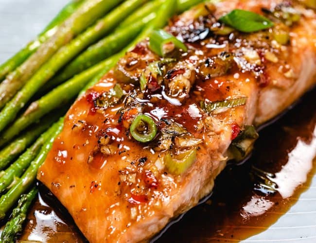 glazed salmon on a plate with asparagus next to it.