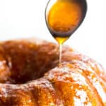 a close up image of a spoon drizzling orange glaze onto a orange Bundt cake.