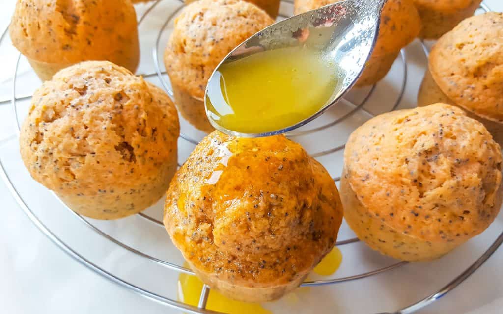 orange poppy seed cakes with an orange juice glaze being poured over with a spoon.