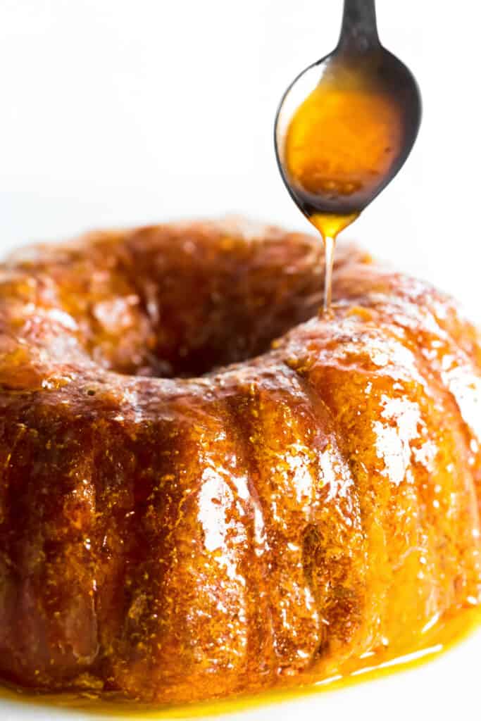 a spoon drizzling orange glaze onto a orange Bundt cake.