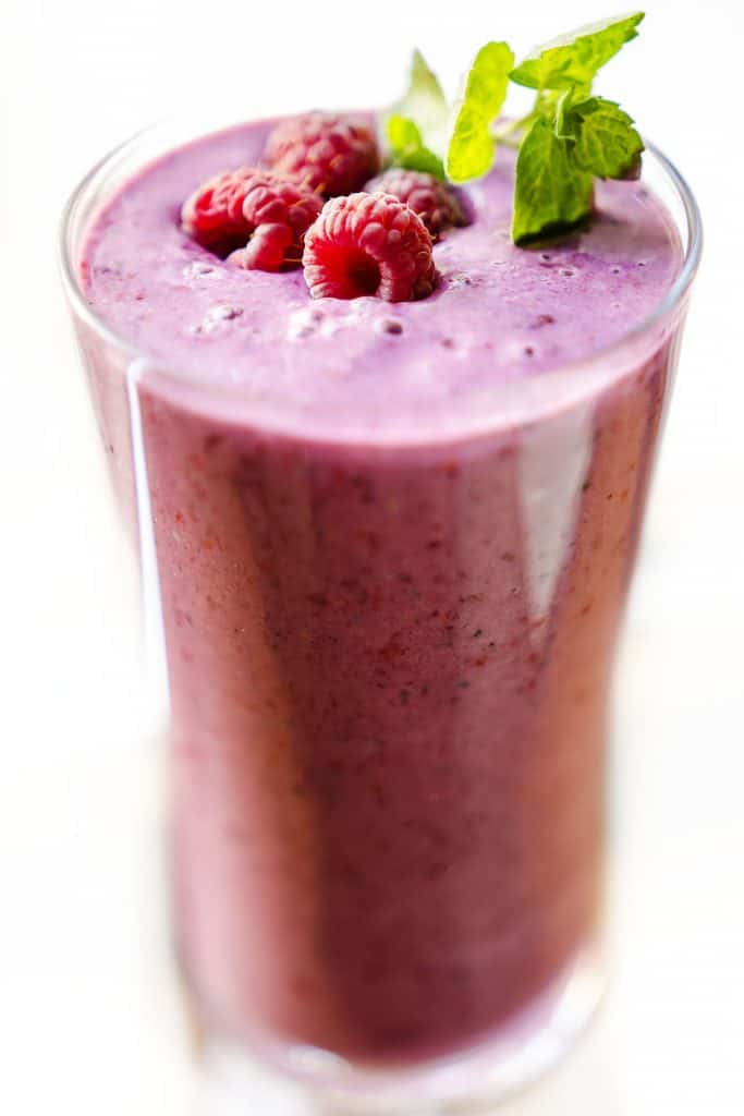 a glass of raspberry smoothie with raspberries and mit