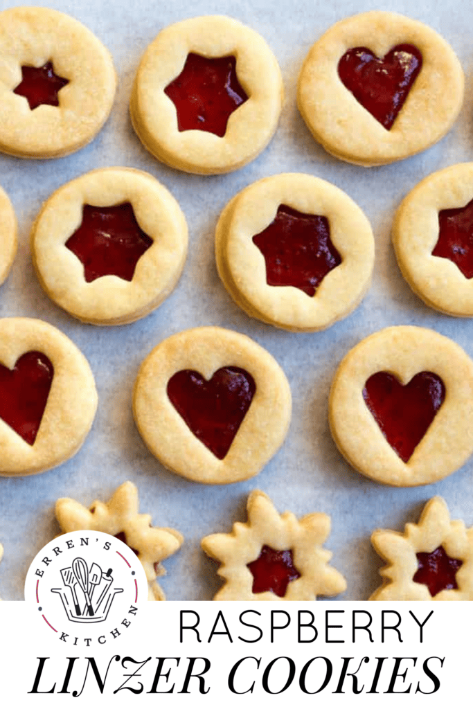 Linzer cookies with raspberry jam and heart, star, and snowflake cut outs are lined up in rows.