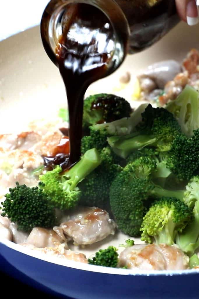 stir-fry sauce being poured into the pan with the chicken and broccoli mixture