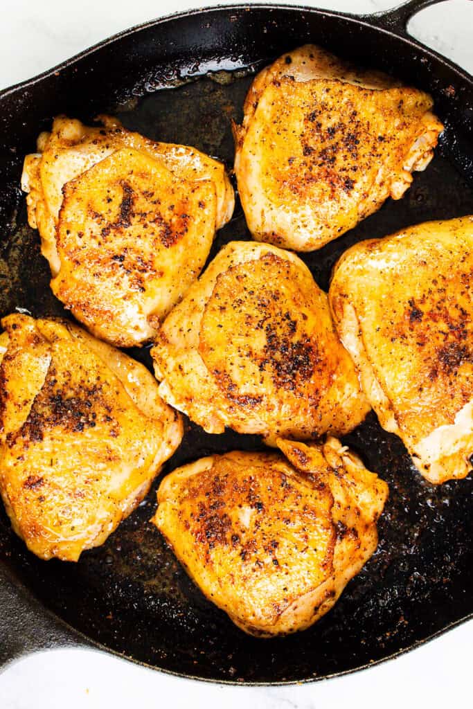 Golden-brown Moroccan chicken thighs seasoned with aromatic spices, cooked to crispy perfection in a cast iron skillet. The chicken appears juicy and flavorful, arranged in a circular pattern.