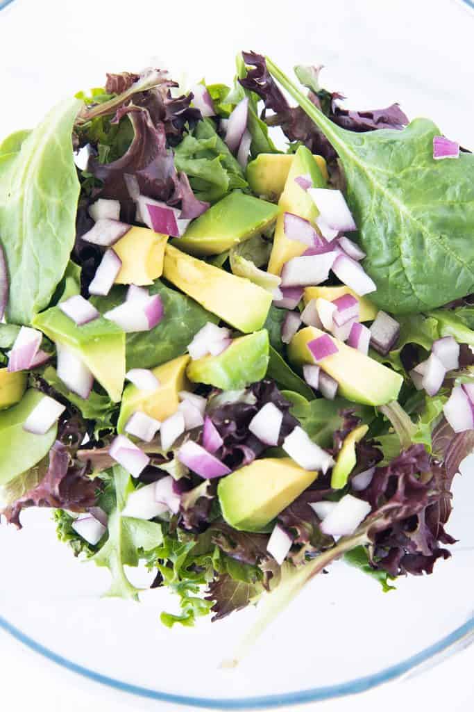 salad greens, red onion and diced avocado in a bowl