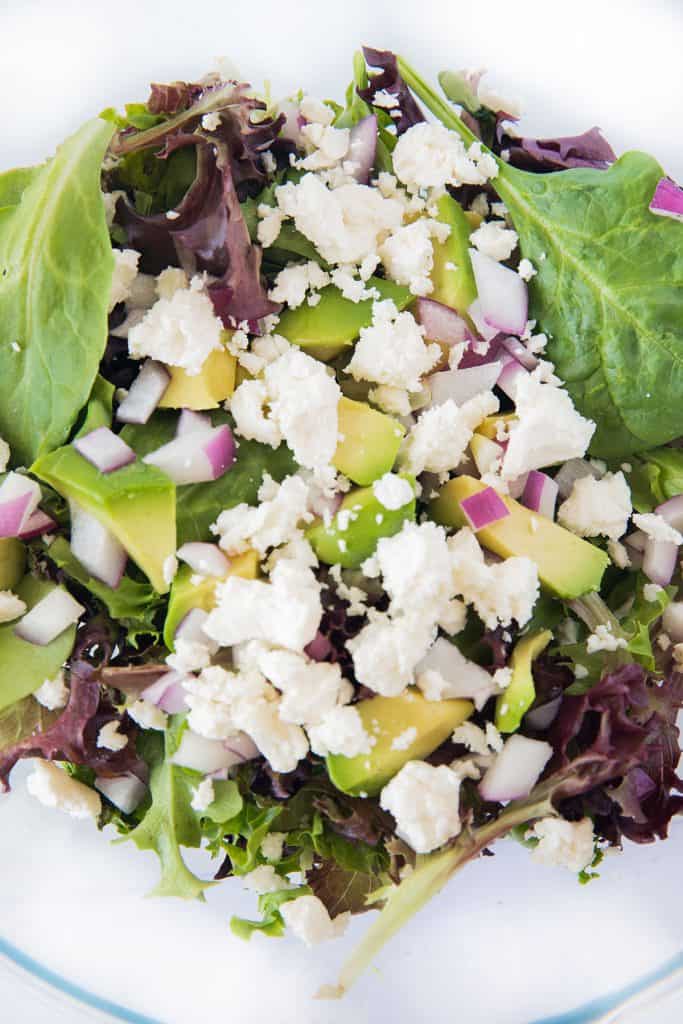 a bowl with salad greens, avocado, red onion and feta cheese