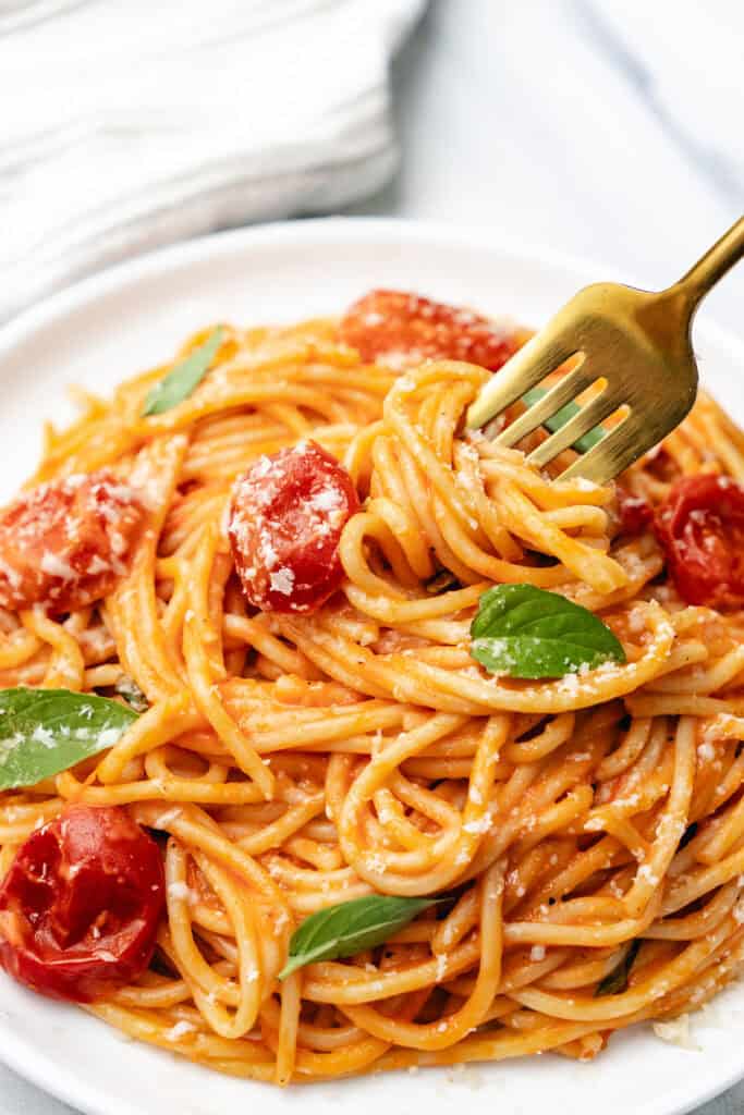 A white plate with a serving of spaghetti with tomato sauce and basil leaves.