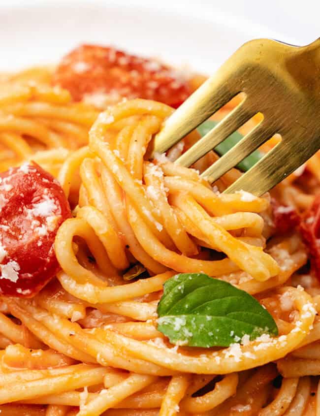 A white plate with a serving of spaghetti with tomato sauce and basil leaves.