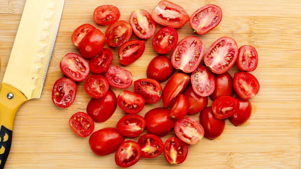 A chopping board with a dozen cherry tomatoes cut in half.