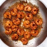 Cooked shrimp with seasoning in a circular arrangement in a pan, showing a golden-brown sear, ready to be served.