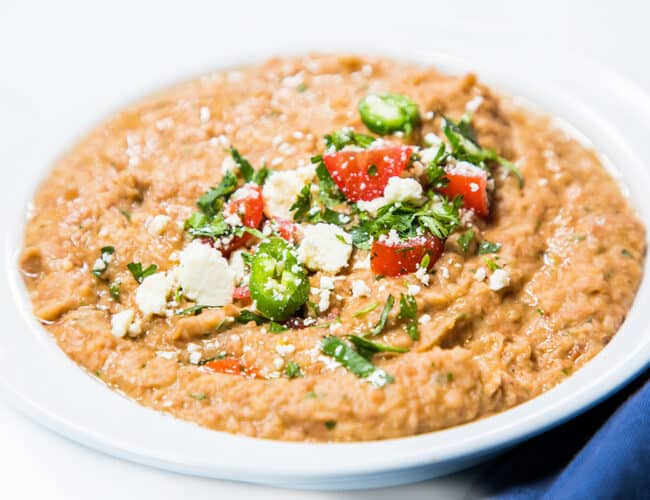 A bowl of refried beans topped with jalapenos, tomatoes, and crumbled cheese.