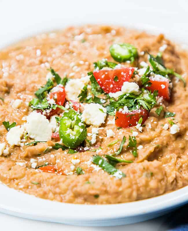 A bowl of refried beans topped with jalapenos, tomatoes, and crumbled cheese.