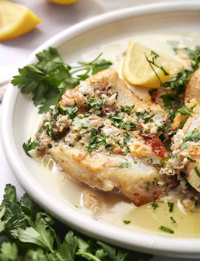 A close up image of Cod in garlic butter sauce with lemon slices