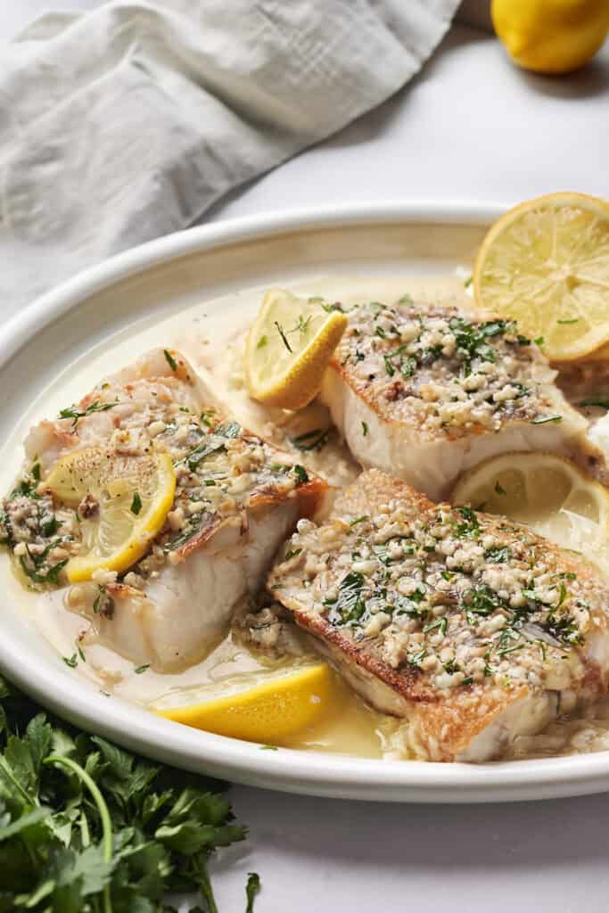 Cod in garlic butter sauce with lemon slices on a white plate