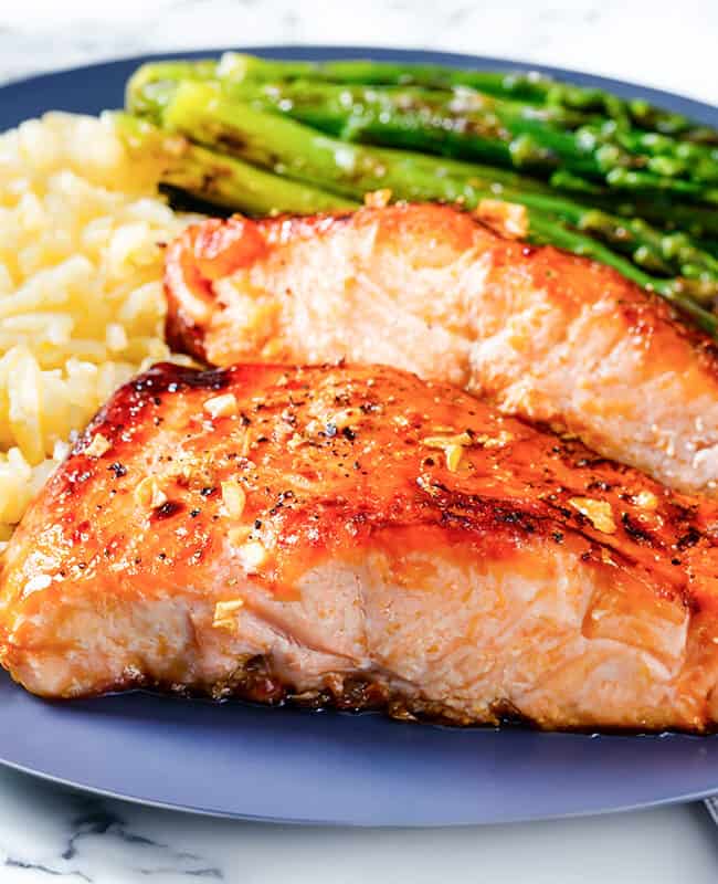 two pieces of garlic butter salmon with roasted asparagus and rice pilaf.