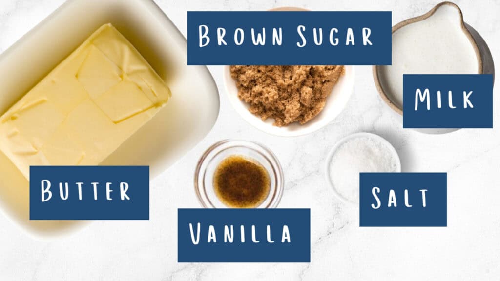 Overhead shot of ingredients for a caramel icing glaze on a white marble surface. Labeled: butter (sliced in a dish), brown sugar (in a bowl), milk (in a small jug), vanilla (in a glass container), and salt (in a small bowl).