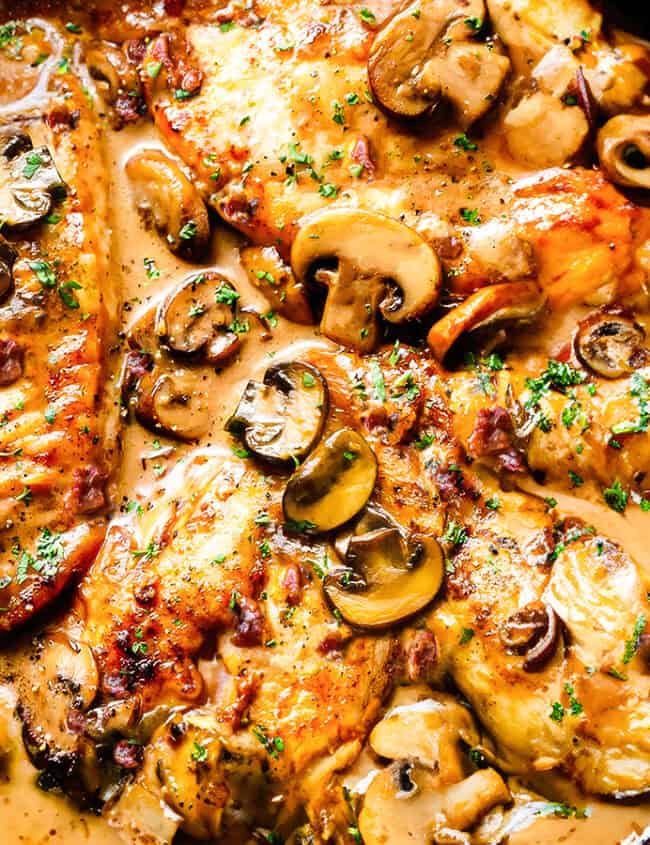 A close up image of A cast iron pan filled with chicken marsala and mushrooms.