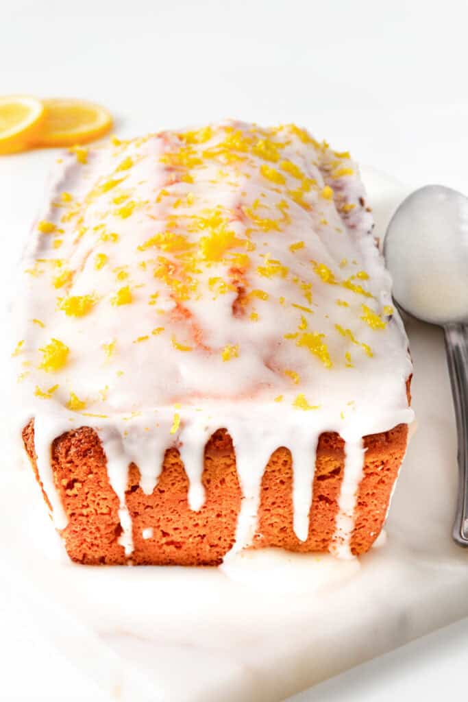 Loaf of lemon pound cake topped with white icing and lemon zest on a cutting board.