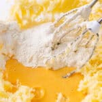 Flour being mixed into creamed butter and eggs with an electric mixer.